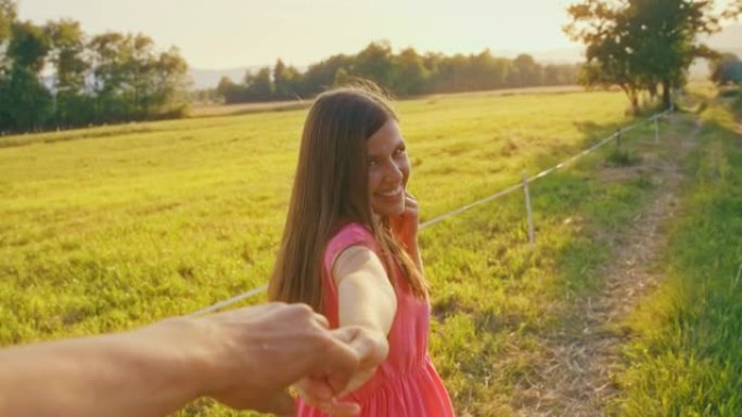 POV微笑的女人牵着男人的手走在阳光明媚的田野上