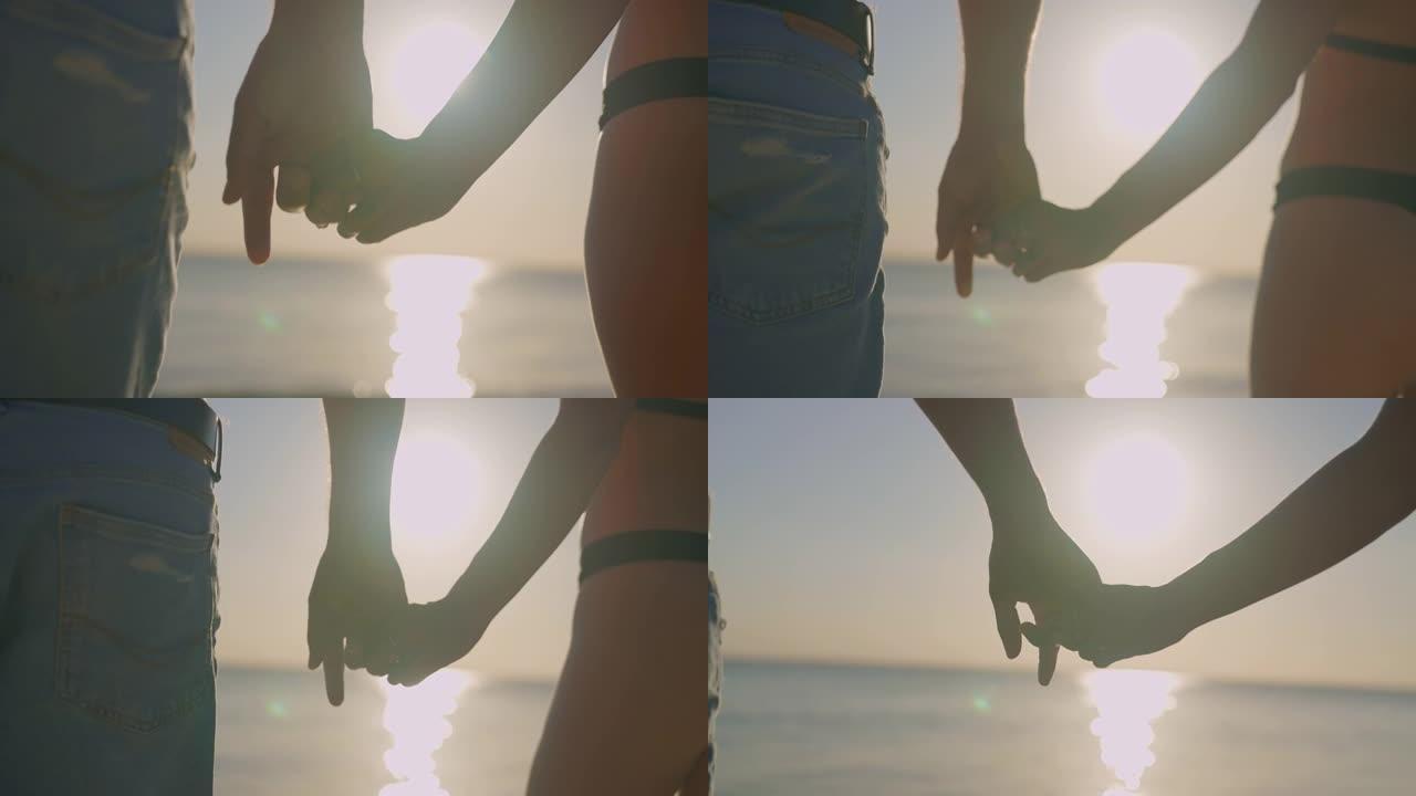 手牵手的夫妇。日落海滩上紫色和橙色天空的深色轮廓。