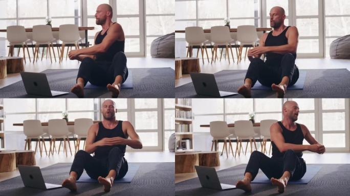 运动男子在家庭锻炼时做腹肌锻炼。使用笔记本电脑