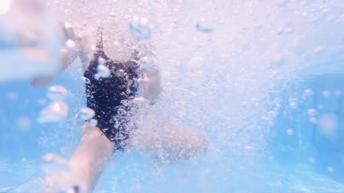 穿着泳衣的女孩在蓝色水池上游泳，水下上升的气泡，慢动作