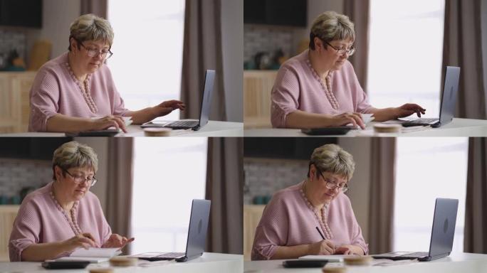 老妇人正在网上学习，通过笔记本电脑在互联网上寻找信息，并在笔记本上做笔记