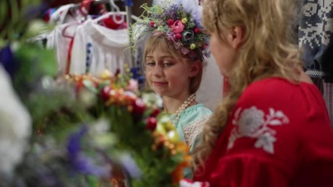 可爱的女孩欣赏手中的花圈，女人在慢动作中说话。漂亮的乌克兰女儿肖像，才华横溢的母亲在室内制作手工工艺
