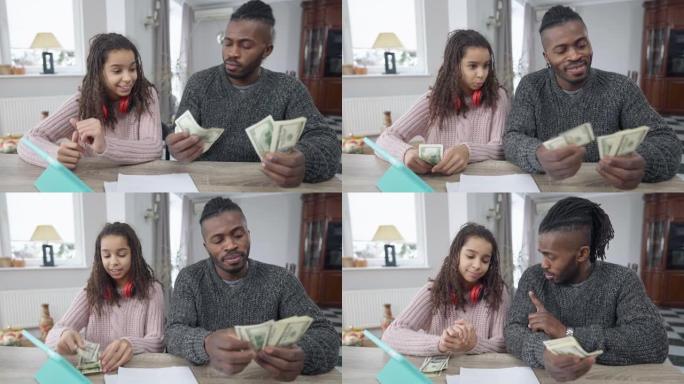 非裔美国富人数钱与坐在客厅桌子旁的少女分享钱的前视图肖像。有钱的单身父亲和十几岁的女儿在家中现金的肖