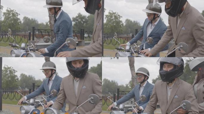 自信的男人和女人在雨中坐在户外的踏板车上。穿着正式服装，头盔和太阳镜在摩托车上摆姿势的高加索骑自行车