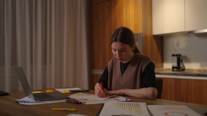 侧视图一名女性在家庭办公室里用笔记本电脑远程工作，并在图表上记录数据，一名商业经济学家分析师。写下做