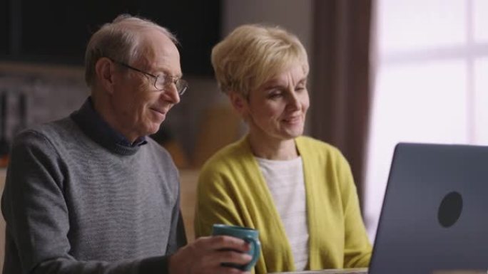 一对已婚老人通过笔记本电脑上的视频聊天与朋友交流，对网络摄像头微笑，肖像