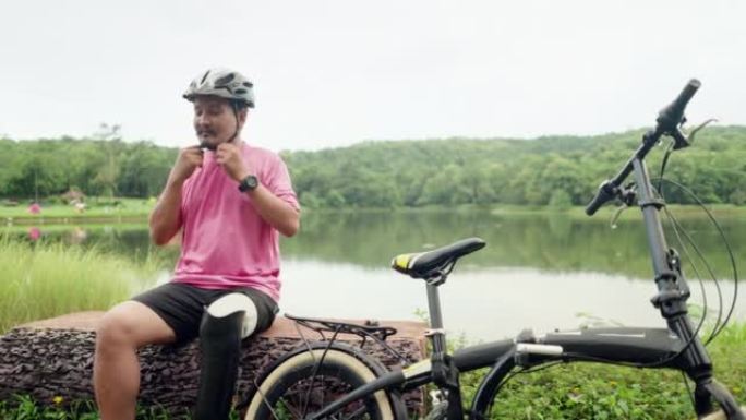 亚洲运动员残疾或截肢者在阳光明媚的夏日骑自行车前戴上自行车头盔。专业男性运动员，腿部假肢练习骑自行车