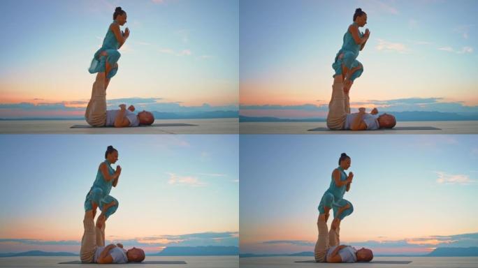 CS女人在黄昏时坐在空中，被她的男瑜伽伴侣的腿抬高在山上