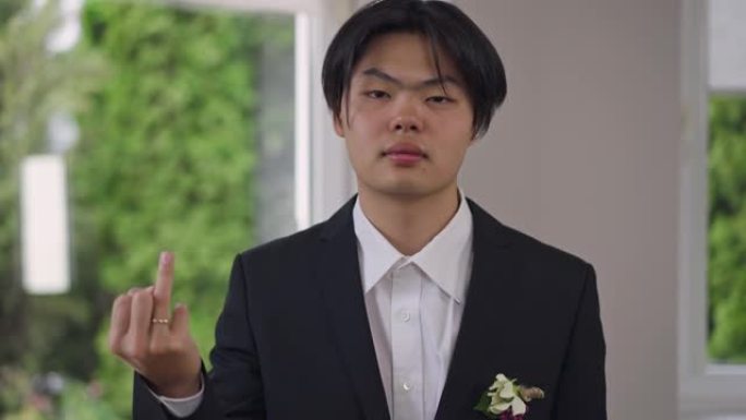 自信的亚洲新郎的肖像，穿着优雅的西装，露出手指，带着结婚戒指看着相机。快乐的年轻人在室内摆姿势。婚姻