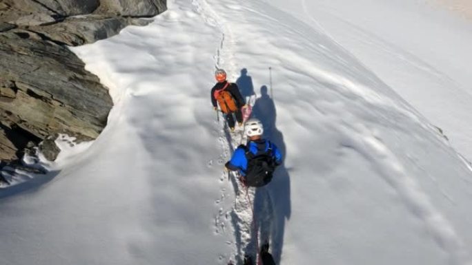 高级登山者团队在欧洲阿尔卑斯山的积雪覆盖的山峰上移动。使用绳索和攀爬设备