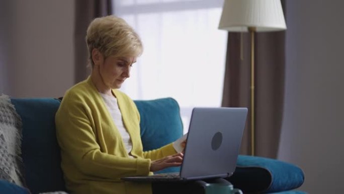 老年妇女正在网上工作，在家中通过互联网在现代笔记本电脑的键盘上打字，在室内进行肖像
