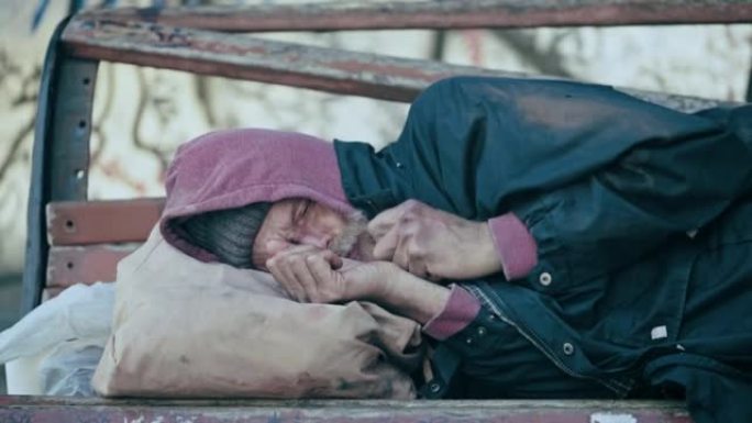 老年男性难民睡在长凳上，试图热身，剥夺了生命