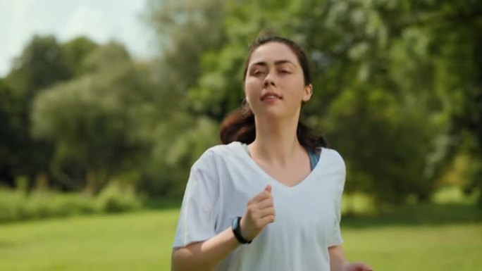 运动和健身。一名年轻女子在公园慢跑，因为呼吸急促而停下来，继续跑步。实时。健康的概念