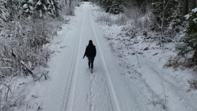 空中无人机拍摄了一名妇女在树林中沿雪道行走的镜头