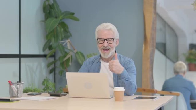 在笔记本电脑上工作的老人竖起大拇指