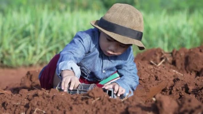 在木薯种植园玩玩具的蹒跚学步的男孩就像一个农民。