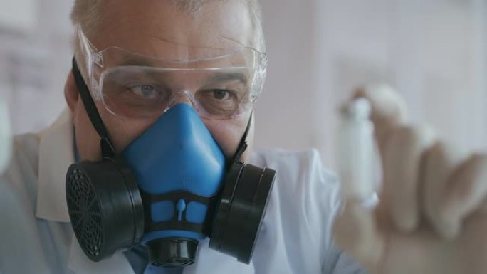 一位戴着蓝色呼吸器和防护眼镜的科学家的极端特写镜头，他开发了一种装有白色粉末安瓿的冠状病毒疫苗。麻醉