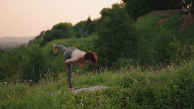 瑜伽大师做平衡和伸展运动。在森林中的山区做瑜伽的女孩的动作的和平与顺畅