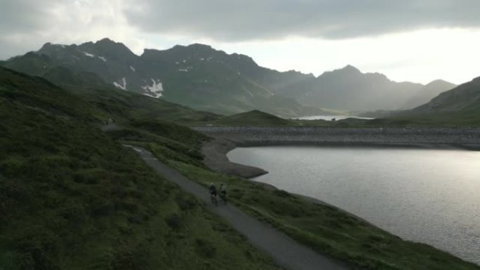 日出时穿越高山草甸小径的山地车者的鸟瞰图