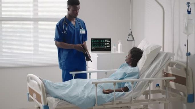 一名黑人男性医生正在与一名躺在医院病床上并与酸供应相连的黑人女性患者交谈。主治医师在医院与患者讨论治