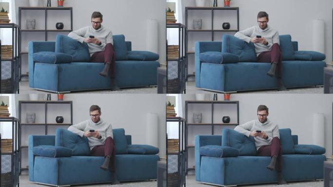 单身男子独自一人坐在家里，用智能手机玩游戏，在客厅的沙发上休息