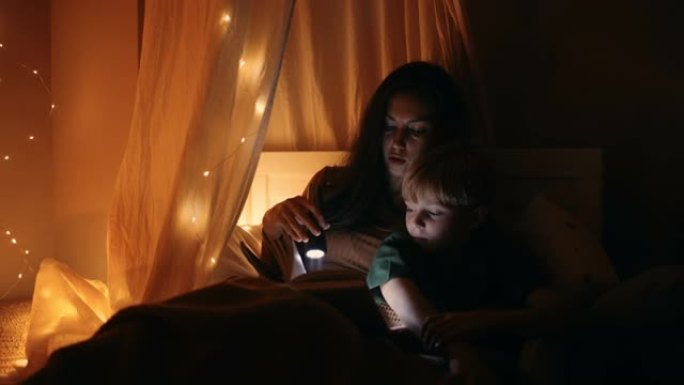 一位母亲和儿子躺在床上，在提着灯笼睡觉前给他读了一个童话。和我儿子一起读一本书，摇篮曲。母亲和儿子在