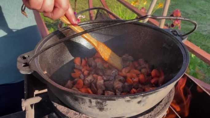 厨师用木铲在明火上的大锅中搅拌肉的手的特写镜头。
