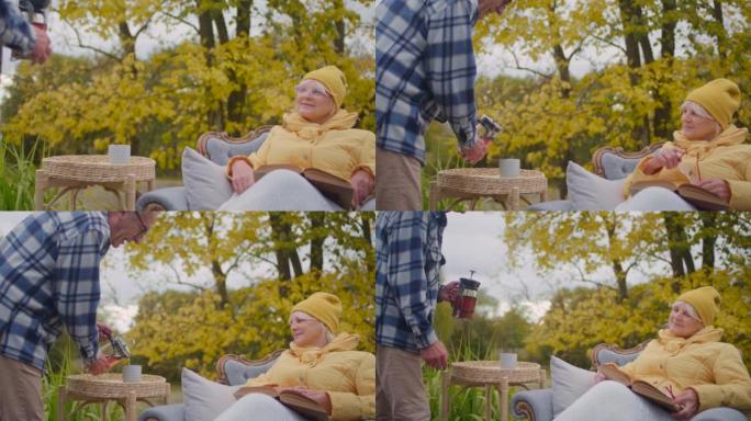 生病的老年妇女病人在外面的椅子上看书。由丈夫照顾