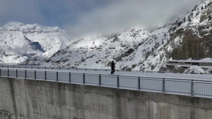 空中无人机拍摄的一名男子穿越山区积雪覆盖的大坝