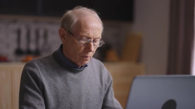 家用厨房里有笔记本电脑的老人的中等肖像，退休人员正在上网，打字和发信息
