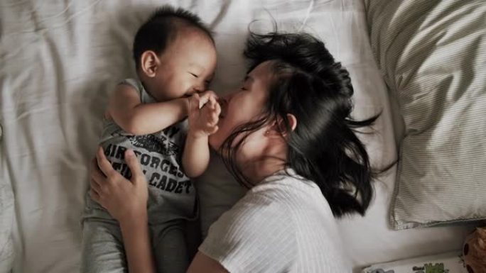 年轻的母亲在床上和一个可爱的男婴玩得开心