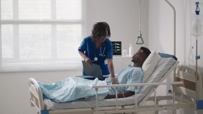 一名黑人女医生正在与一名躺在医院病床上并与酸供应相连的黑人男性患者交谈。
