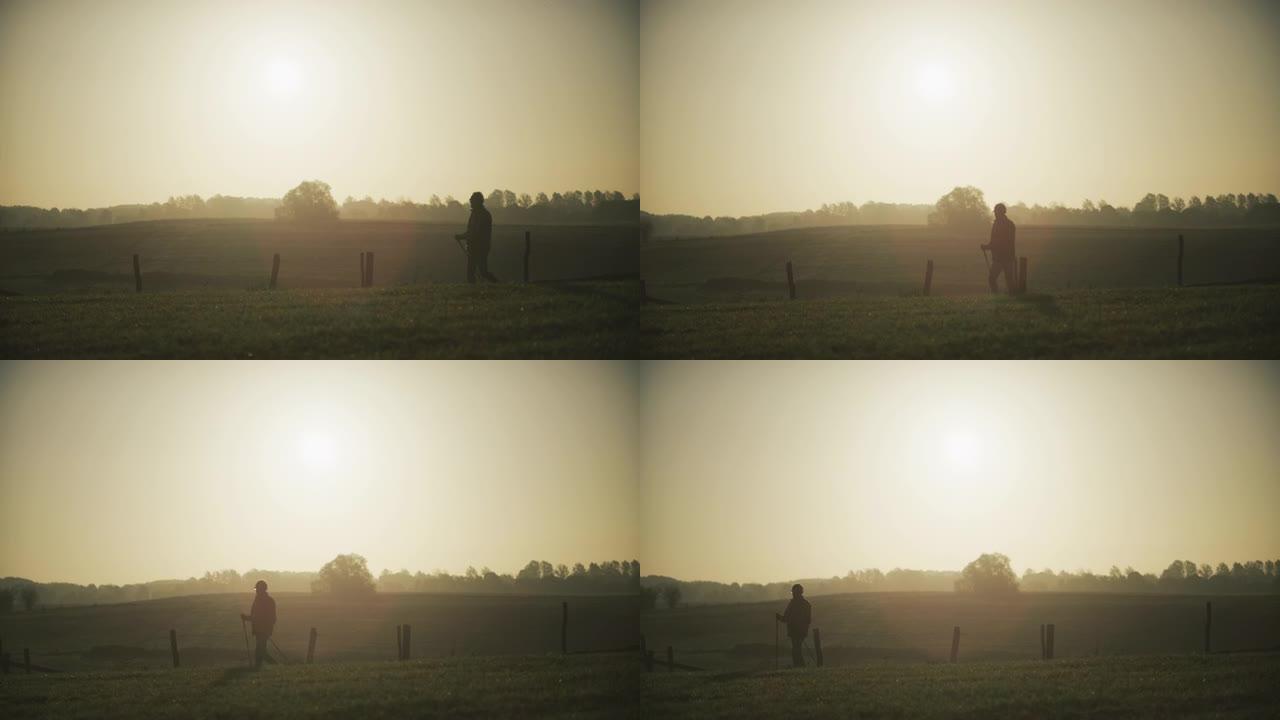 老人北欧人在升起的金色太阳下，带着晨露在绿色的草地上行走
