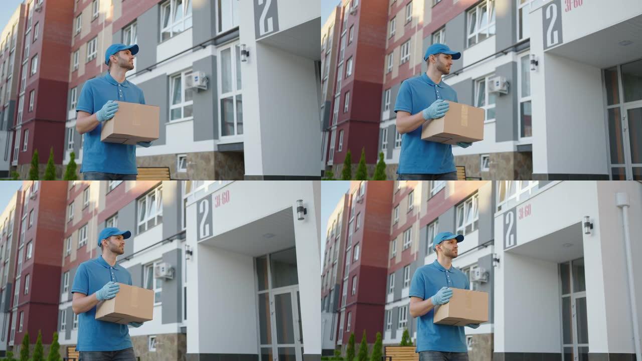 高加索年轻漂亮的男人，穿着蓝色帽子的送货员走在街上，拿着纸箱，同时使用智能手机，寻找路线。男性快递员