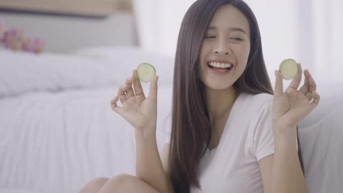 微笑的年轻女子在眼睛上拿着黄瓜片