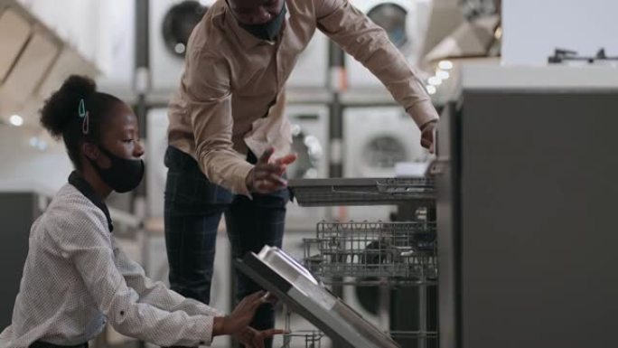年轻的非洲裔美国配偶正在家用电器商店选择洗碗机，男人和女人正在查看厨房设备