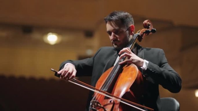 穿着黑色西装的才华横溢的大提琴手正在歌剧院现场演奏大提琴，交响乐队的排练