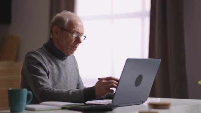 老人在家在线学习，退休人员的自我教育，老人正在使用笔记本电脑，在互联网上寻找信息