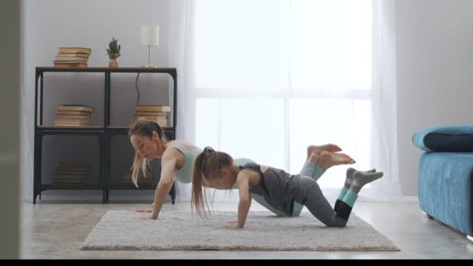运动女人正在训练她的孩子做俯卧撑，母亲和女儿在公寓里一起训练