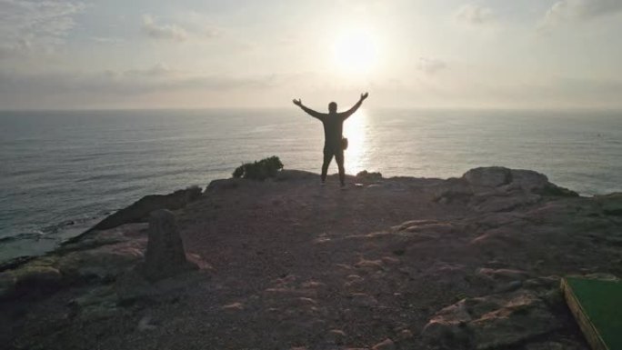 成功的人举手示意成功。到达顶峰的幸福。海边岩石上的轮廓。