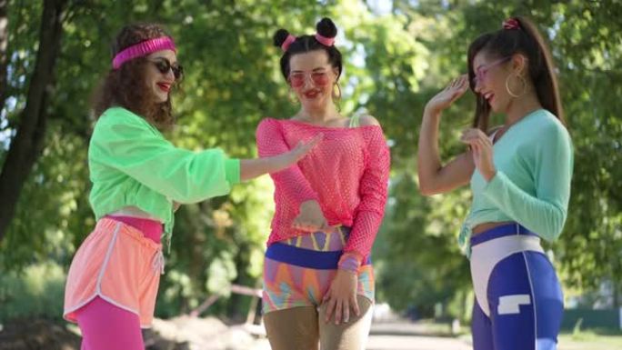 三个穿着复古衣服的快乐女性朋友戴上墨镜，双手慢动作离开。微笑迷人的高加索女性在夏日公园享受户外休闲。