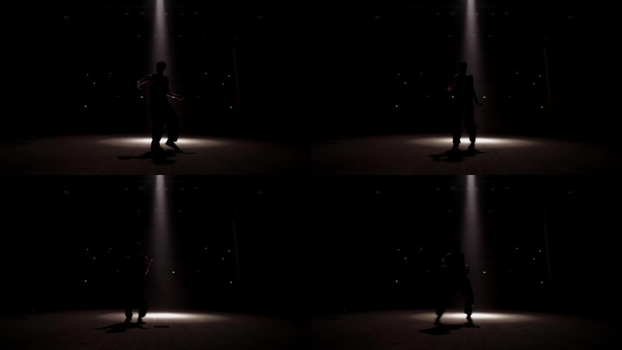 十几岁的男孩在黑暗的工作室里跳舞嘻哈舞蹈，b-boy的剪影与聚光灯雷