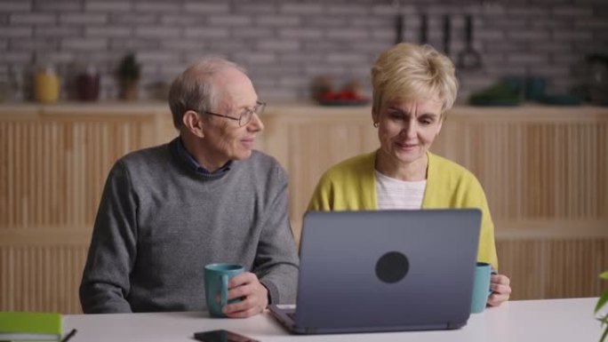 与朋友或家人的在线视频聊天，祖父和祖母的肖像看着笔记本电脑的显示器，坐在家里的厨房里