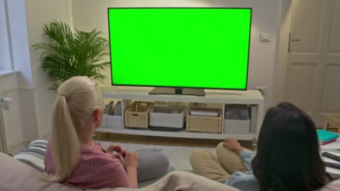 DS两个女人坐在客厅的沙发上，一边看电视一边聊天