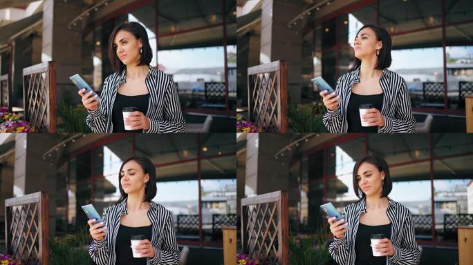 一只手拿着咖啡杯，另一只手拿着智能手机的女人，夏天在城市的露天咖啡馆里肖像