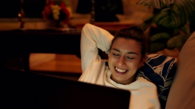美丽的年轻女子在沙发上放松。在笔记本电脑上观看有趣的电影