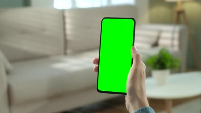 手机上女性的视点视图，绿屏为复制空间。没有跟踪标记的Chromakey模型。20多岁的女士在沙发上观
