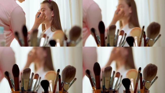 女人脸画家通过画笔前景为模特女孩化妆。
