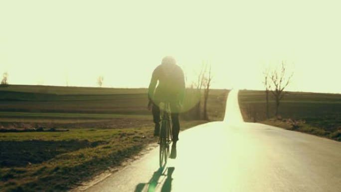 男性公路自行车手在空旷的地方超速行驶的背光轮廓。春天的日落