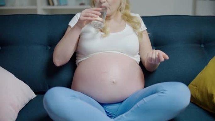 Blond pregnant woman taking vitamin, drinking wate
